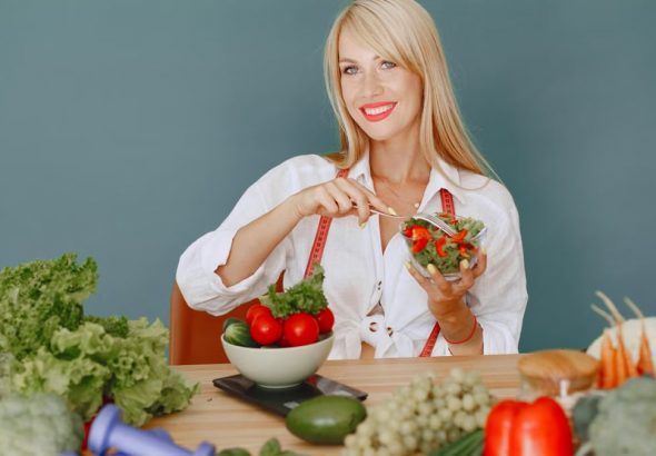Blonde woman enjoying a fresh salad surrounded by vegetables, promoting healthy eating.