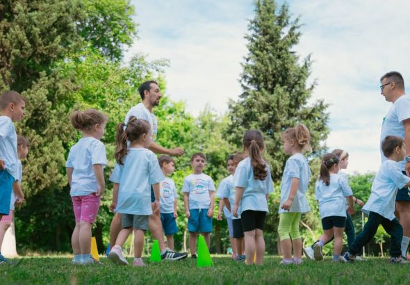 Group of children and teachers playing and learning in a sunny park setting.
