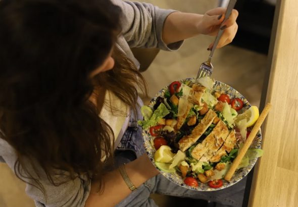 Overhead view of a woman eating a chicken salad balancing health with deliciousness.